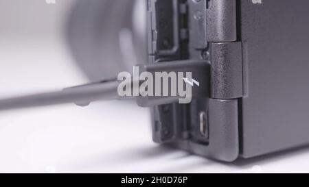 Close-up of wired charging of black electronic device. Action. Charging wire is connected to discharged camera. Charging and importing photos from cam Stock Photo