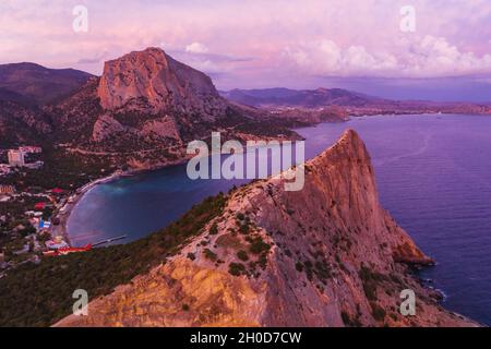 Pink sunset in Novyi Svit in autumn with mount Falcon in background. Sudak, the Republic of Crimea. Aerial view. Stock Photo