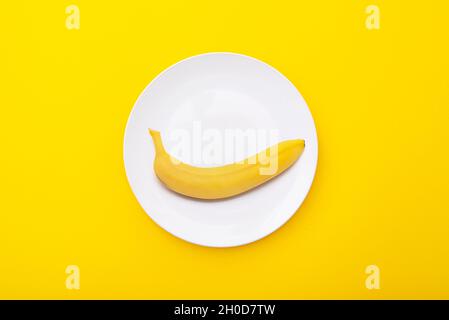 Bright yellow banana on white ceramic plate. Creative minimal composition with riple banana, top view Stock Photo