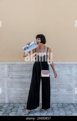 Portrait of happy young woman wearing elegant black jumpsuit, holding large liquor flask Stock Photo