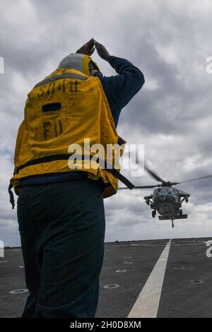 210129-N-UM706-1489 PHILIPPINE SEA (Jan. 29, 2021) Boatswain’s Mate 2nd Class Jeremiah Nortey, from Bronx, N.Y., signals an MH-60S Sea Hawk helicopter, from Helicopter Sea Combat Squadron (HSC) 25, aboard the amphibious dock landing ship USS Ashland (LSD 48). Ashland, part of the America Expeditionary Strike Group, along with the 31st Marine Expeditionary Unit, is operating in the U.S. 7th Fleet area of responsibility to enhance interoperability with allies and partners, serving as a ready response force to defend peace and stability in the Indo-Pacific region. Stock Photo