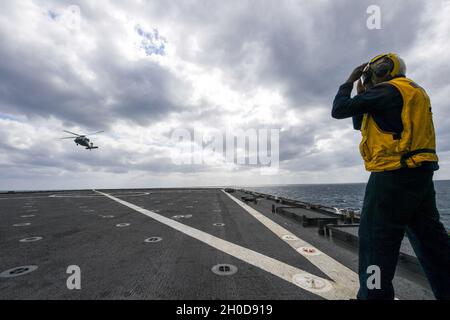 210129-N-UM706-1342 PHILIPPINE SEA (Jan. 29, 2021) Boatswain’s Mate 2nd Class Jeremiah Nortey, from Bronx, N.Y., signals an MH-60S Sea Hawk helicopter, from Helicopter Sea Combat Squadron (HSC) 25, aboard the amphibious dock landing ship USS Ashland (LSD 48). Ashland, part of the America Expeditionary Strike Group, along with the 31st Marine Expeditionary Unit, is operating in the U.S. 7th Fleet area of responsibility to enhance interoperability with allies and partners, serving as a ready response force to defend peace and stability in the Indo-Pacific region. Stock Photo