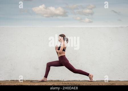 Sporty woman practicing yoga and keeping fit outside. Crescent pose with hands to heart centre. Stock Photo