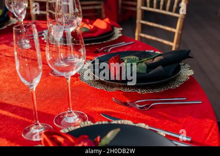 Guests table setting for banquet in black, red and gold style. Elegant and luxury dinner arrangement: decor, tablecloth, plates with napkins and fresh Stock Photo