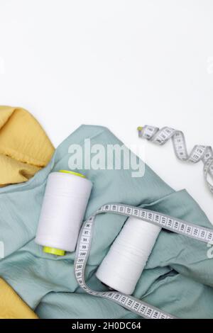 Various fabrics, measuring tape and thread isolated on white. Flat lay Stock Photo
