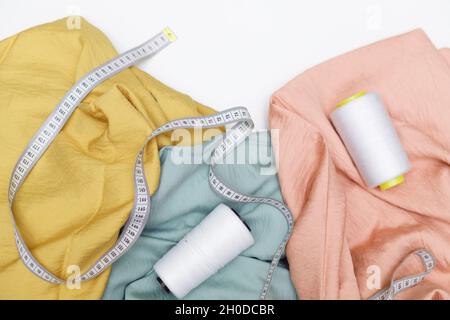 Various fabrics, measuring tape and thread isolated on white. Flat lay Stock Photo