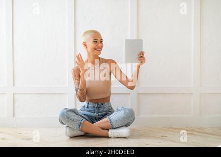 Modern communication concept. Young lady video calling via digital tablet, waving hand to webcam over white wall Stock Photo