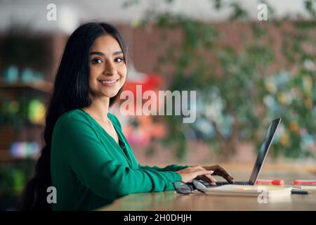 Side view of happy indian lady freelancer working from cafe Stock Photo