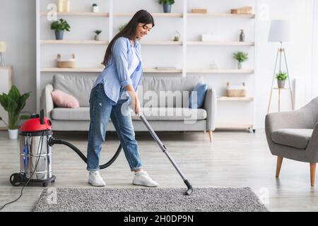 Cheerful woman cleaning rug carpet with vacuum cleaner Stock Photo