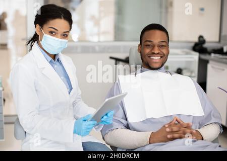Dental Insurance Concept. Black Dentist Woman And Male Patient Posing In Clinic Stock Photo