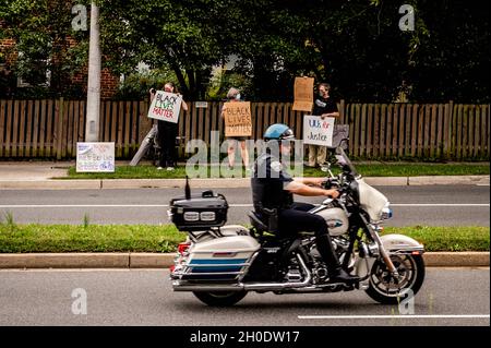 Motorcycle police officer passing protesters with signs Stock Photo