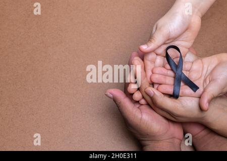 Woman hand holding a light pink ribbon on a pink background - cancer symbol  Stock Photo by wirestock