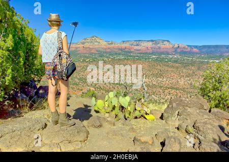 A young woman taking a cell phone photo of the Sedona landscape in Arizona like other typical tourists. In the background is Thunder Mountain and Coff Stock Photo