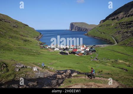 Hikers walking down a hill towards the village of Tjornuvik,  Streymoy Island, Faroe Islands,Scandinvia, Europe Stock Photo