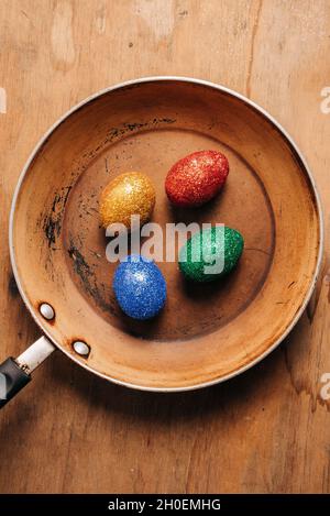 Eggs covered in colorful glitter in an old cooking pan on wooden table Stock Photo