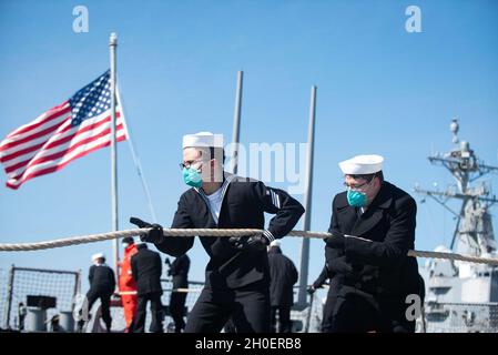 210217-N-QD512-1356 NORFOLK (Feb. 17, 2021) Sailors heave in mooring lines before departing Naval Station Norfolk aboard the Arleigh Burke-class guided-missile destroyer USS Mitscher (DDG 57) Feb. 17, 2021. Mitscher is operating in the Atlantic Ocean in support of naval operations to maintain maritime stability and security in order to ensure access, deter aggression and defend U.S., allied and partner interests. Stock Photo