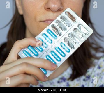 A young girl or woman holding and shows a blue complex of vitamins and minerals in capsules in her hand. Focus on the face and the pills Stock Photo