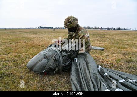 A US Army Paratrooper assigned to 1st Battalion, 503rd Infantry Regiment, 173rd Airborne Brigade secures his equipment after an airborne operation from U.S. Air Force 86th Air Wing C-130 Hercules aircraft, during exercise Eagle Ace II at Rivolto Italian Air Force Base, Udine Italy, Udine Italy, Feb. 18, 2021 under Covid-19 prevention conditions.  The purpose of this operation is to improve relationship with host nation, strengthen the alliance and increase NATO interoperability. The 173rd Airborne Brigade is the U.S. Army Contingency Response Force in Europe, capable of projecting ready forces Stock Photo