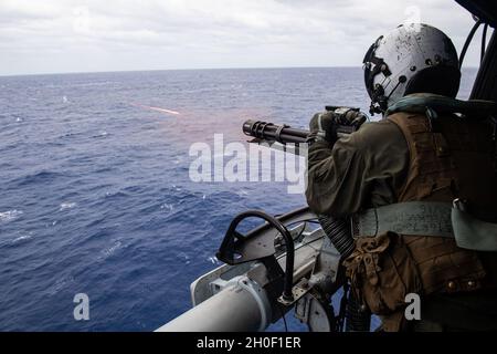 PHILIPPINE SEA (Feb. 19, 2021) Sgt. Aaron Tidwell, from Seattle, fires a GAU-17 minigun from a UH-1Y Huey helicopter assigned to Marine Medium Tiltrotor Squadron (VMM) 262 during a live-fire training exercise. VMM 262 is operating with the America Expeditionary Strike Group and the 31st Marine Expeditionary Unit in the U.S. 7th Fleet area of responsibility to enhance interoperability with allies and partners and serve as a ready response force to defend peace and stability in the Indo-Pacific region. Stock Photo