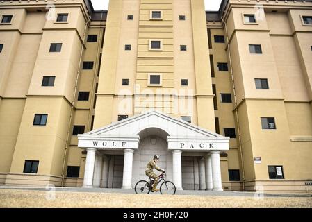 An Airman cycles past a dormitory at Kunsan Air Base, Republic of Korea, Feb. 22, 2021. The dormitories, maintained and monitored by the 8th Civil Engineer Squadron, were built between 1950 and 2006, and have the capacity to house more than 3,000 service members. The 8th CES, also known as the Red Devils, recently completed a study to improve the Wolf Pack’s quality-of-life and mission accomplishment. The study focused on infrastructure and utilities like dormitories, heating, ventilation, and air conditioning systems, water supply and treatment, military working dog kennels, and even game-pla Stock Photo