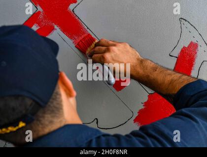 CAPE TOWN, South Africa (Feb. 23, 2021) Boatswain’s Mate Seaman Jorge Loli paints the Boatswain’s Mate rating badge on a bulkhead while on board the Expeditionary Sea Base USS Hershel “Woody” Williams (ESB 4) in Cape Town, South Africa, Feb. 23, 2021. Hershel “Woody” Williams is operating in U.S. Sixth Fleet to conduct interoperability training and build strategic partnerships with their African partners. Stock Photo