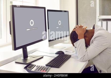 Woman sitting in front of office computers and waiting for software update to install Stock Photo