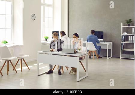 Modern interior of company's workplace with employees sitting at tables with laptops. Stock Photo