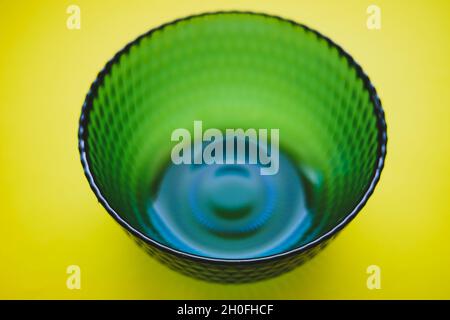 Blue glass bowl on a yellow table. Mixing blue and yellow colors gave a green tint. Stock Photo