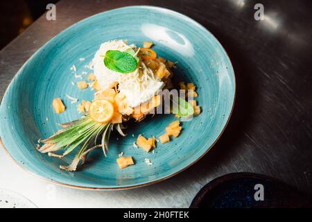 Freshly prepared salad lies inside the pineapple, which is cut lengthwise, sprinkled with grated cheese. Everything looks very appetizing. Stock Photo