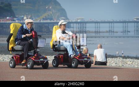 ELDERLY PEOPLE RIDING MOBILITY SCOOTERS ON THE SEAFRONT OF LLANDUDNO WALES UK RE RETIREMENT GOLDEN YEARS HOLIDAYS  MARRIAGE COUPLES ETC Stock Photo