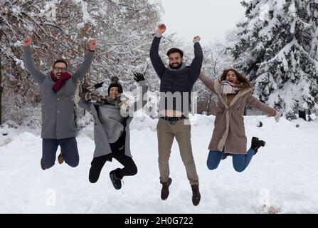 Group of young people jumping and having fun on snow in forest Stock Photo