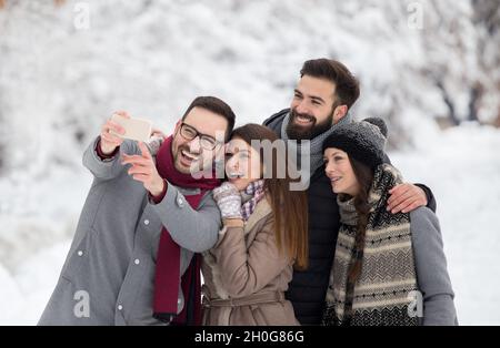 Group of friends taking selfie in snowy forest, enjoying winter holidays Stock Photo