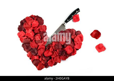 Red petals shaped into a heart with a knife sticking in with loose petals representing drops of blood, taken on a plain white background