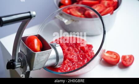 Old metal vintage manual meat grinder, plate with chopped tomatoes,pot with tomatoes on a white table. Making homemade adjika, home preservation, ferm Stock Photo