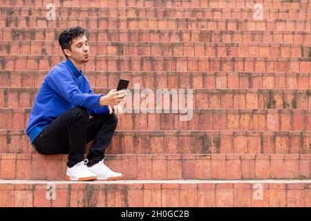 Man taking a selfie with a funny expression. Orange and blue. Man wearing a blue jumpsuit on orange stairs. Commercial concept for advertising. Stock Photo