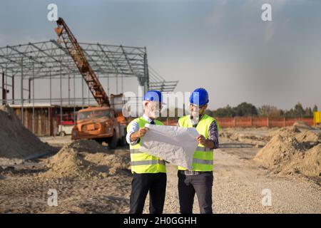 Two satisfied engineers talking at building site with metal construction in background Stock Photo