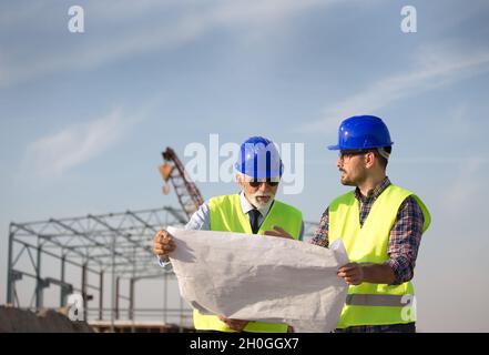 Two satisfied engineers talking at building site with metal construction in background Stock Photo