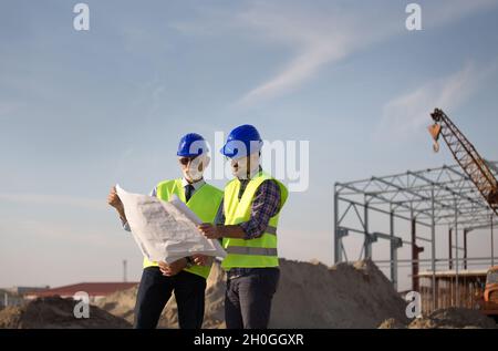 Two satisfied engineers talking at building site with metal construction in background Stock Photo