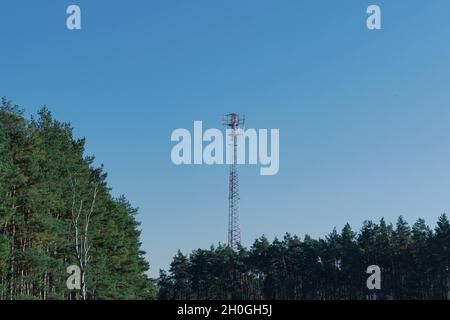 Mast, base station for mobile telephony. The metal structure is painted white and red. A crown with antennae on the top. The sky is clear. Stock Photo