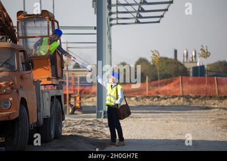Construction worker from crane giving blueprints to an senior engineer on ground at building site Stock Photo