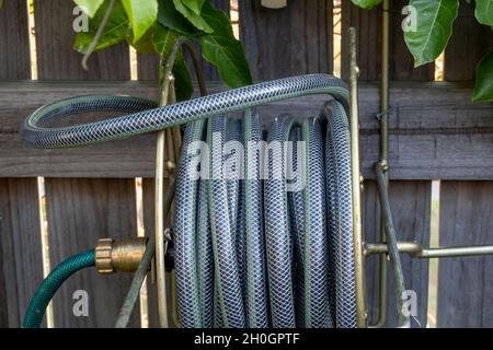 A rolled up hose on a reel in a garden with a timber fence background Stock Photo