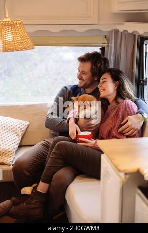 Young married couple inside trailer or camper sit on sofa cuddling cute dog enjoy weekend together Stock Photo