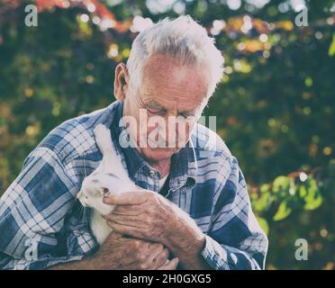Senior man with little white cat in garden Stock Photo