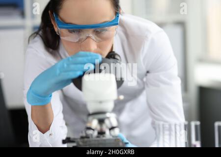 Young woman scientist with glasses looks through microscope closeup Stock Photo