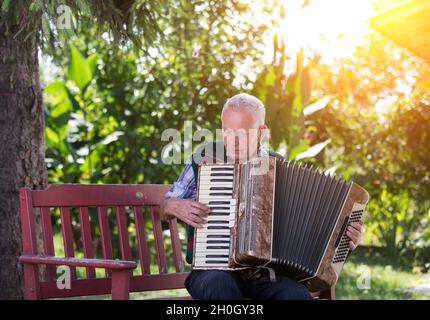 Elderly man playing accordion on bench in garden Stock Photo