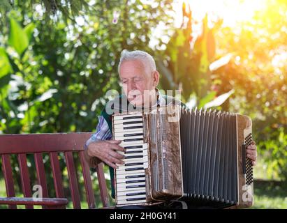 Elderly man playing accordion on bench in garden Stock Photo