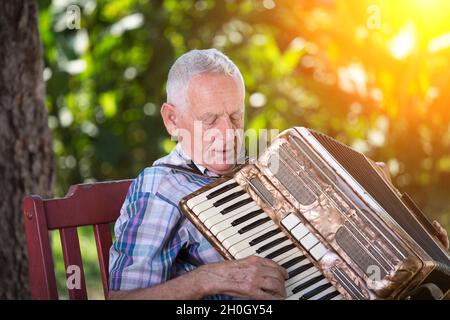 Elderly man playing accordion on bench in garden Stock Photo