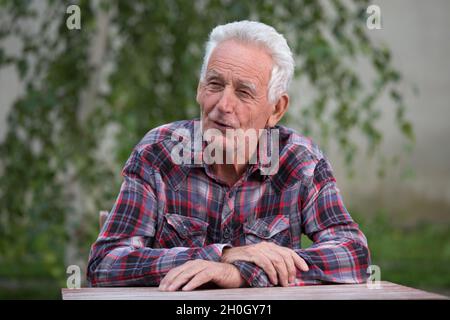 Smilling old man sitting at table in garden Stock Photo