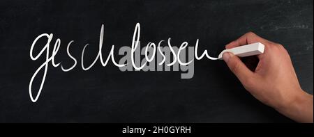 The word close is standing on a blackboard, handwritten with white chalk, german language Stock Photo