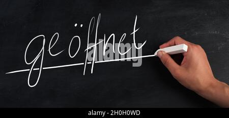 The word open is standing in german language on a chalkboard, handwritten Stock Photo